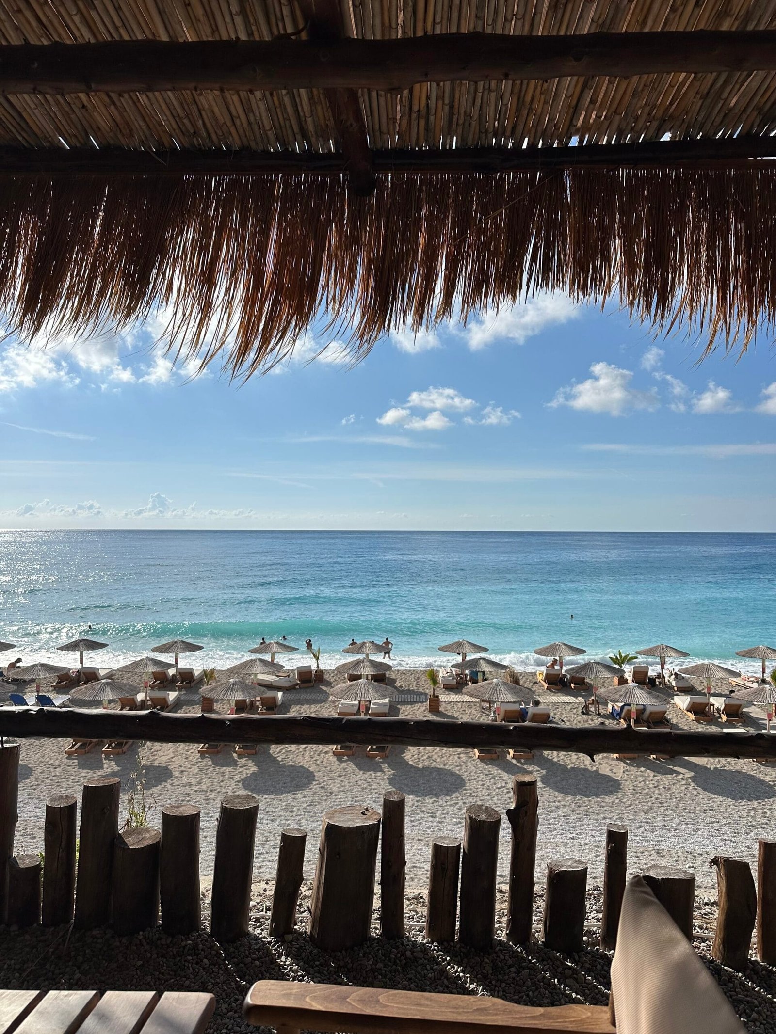 Hidden Beaches in Lefkada 1 A shaded terrace overlooking beach umbrellas, the shoreline and the blue Ionian Sea.